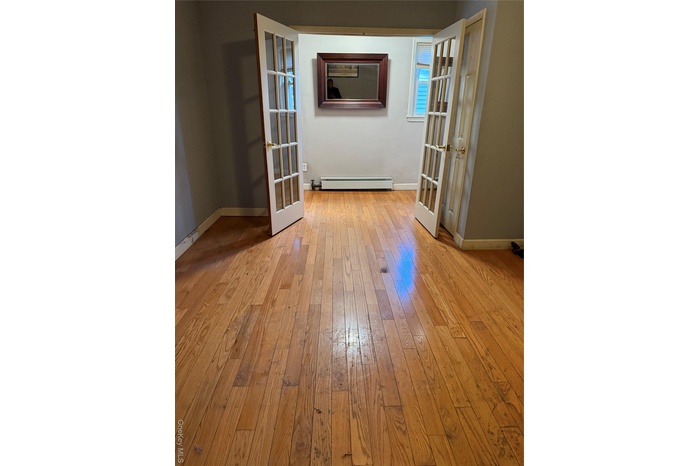Unfurnished room featuring light wood finished floors, french doors, and a baseboard heating unit