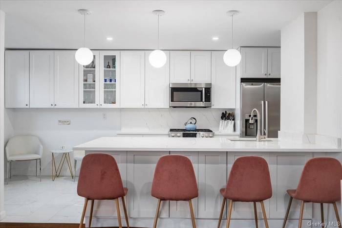Kitchen with a kitchen breakfast bar, glass insert cabinets, white cabinets, light stone counters, and recessed lighting
