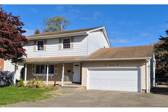 Traditional-style home featuring a garage, a porch, driveway, and a front yard