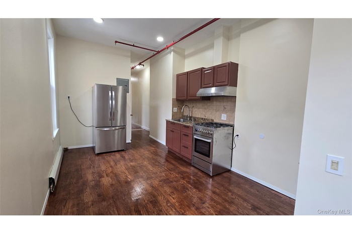 Kitchen with appliances with stainless steel finishes, decorative backsplash, dark wood-style flooring, under cabinet range hood, and a baseboard radi