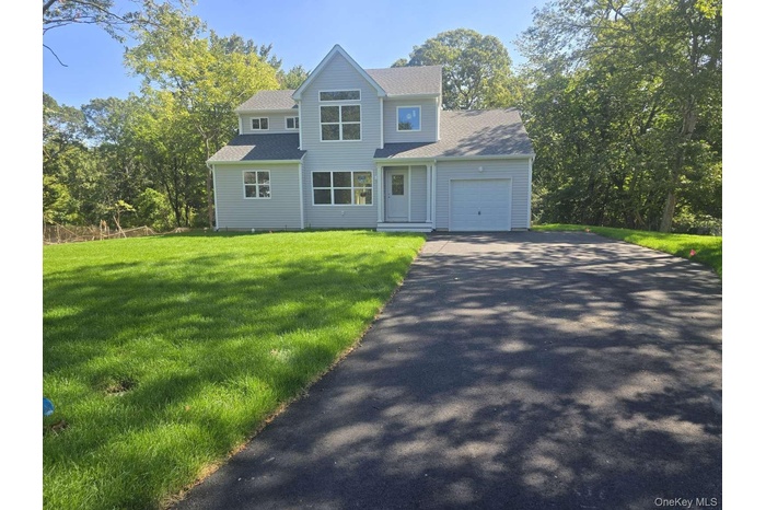 View of front of property with asphalt driveway, a garage, a front lawn, and roof with shingles