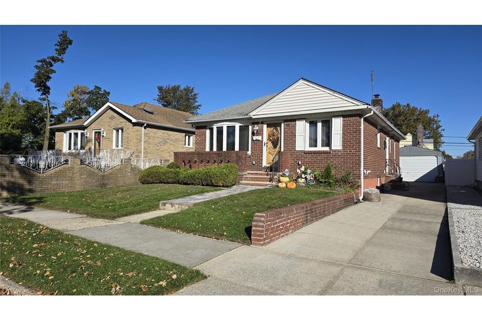 Bungalow-style home featuring a front lawn, brick siding, an outbuilding, a chimney, and a garage