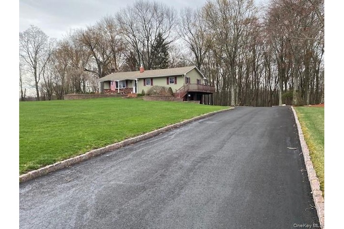 Single story home featuring aphalt driveway, a chimney, and a front lawn