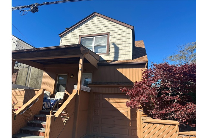View of front facade featuring a wooden deck, a shingled roof, and a garage