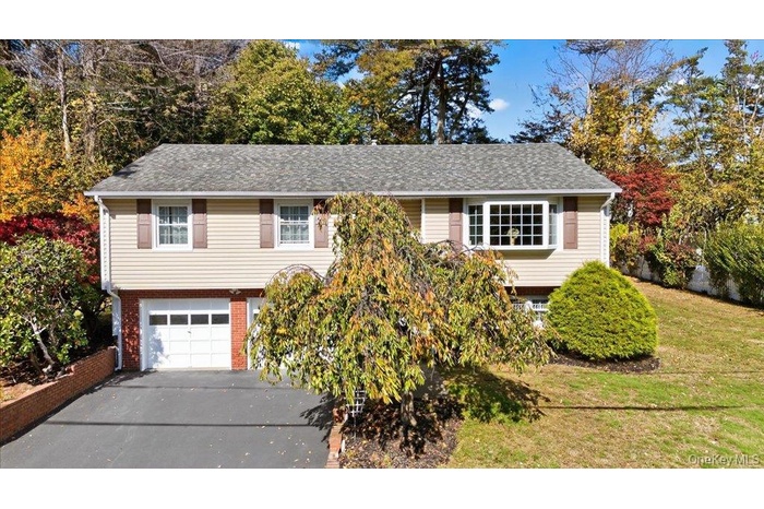Raised ranch featuring brick siding, asphalt driveway, a garage, and a shingled roof