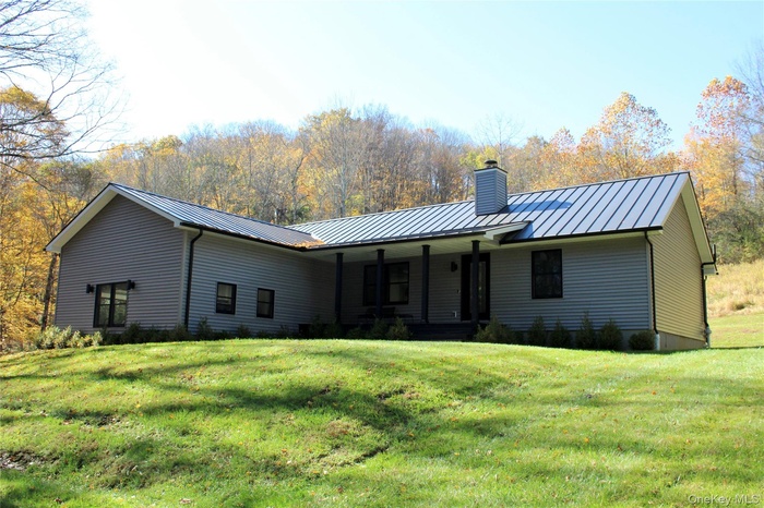 Back of property featuring a chimney, a metal roof, a porch, and a yard