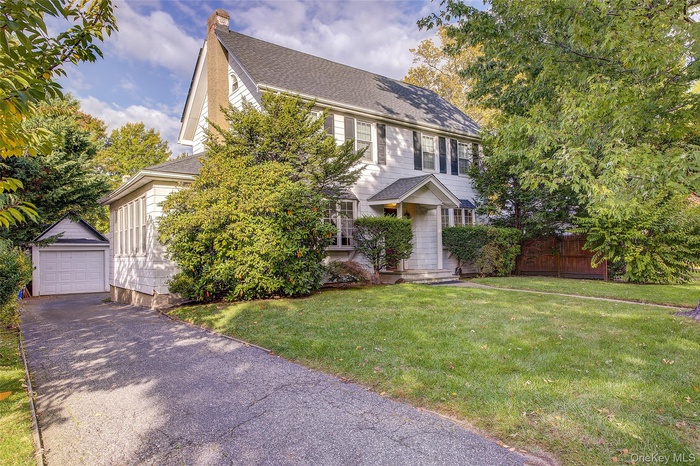 View of front of home featuring an outdoor structure, a shingled roof, a chimney, a garage, and driveway