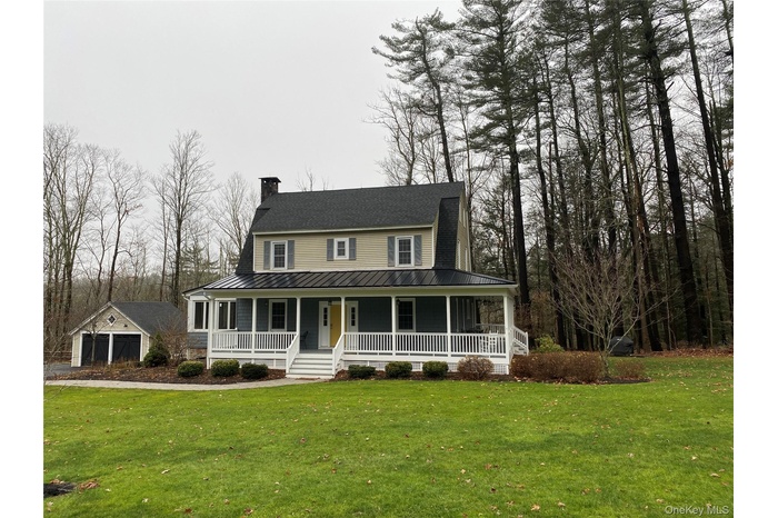 Farmhouse-style home featuring a chimney, a large porch, a front lawn, an outdoor structure, and a metal roof