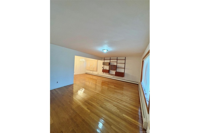 Unfurnished living room featuring a chandelier, light wood-style floors, and baseboard heating