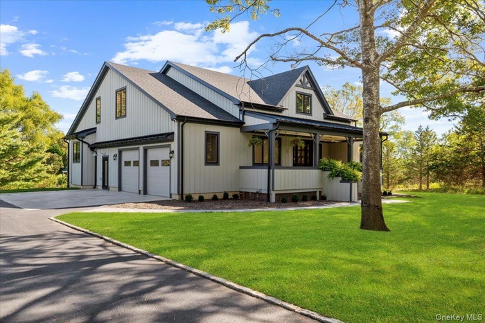 Modern farmhouse featuring a front lawn, a shingled roof, covered porch, a garage, and asphalt driveway