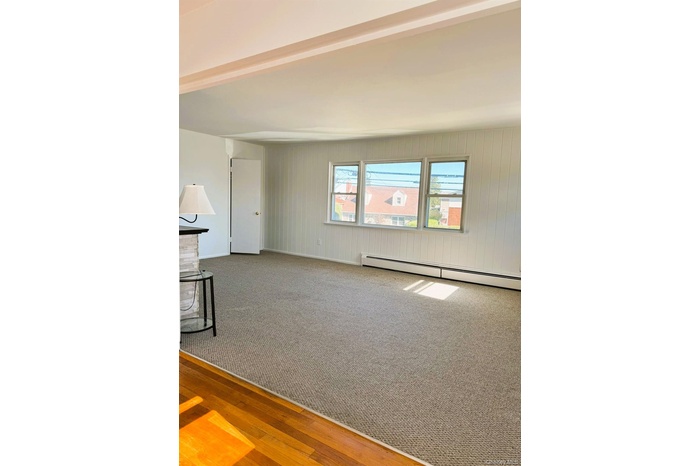 Empty room featuring healthy amount of natural light, a baseboard heating unit, wood finished floors, beamed ceiling, and carpet floors