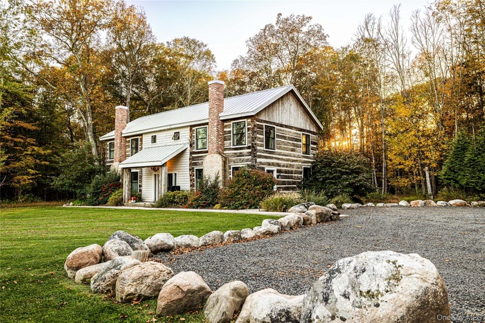 Log-style house with a metal roof, a chimney, view of wooded area, a front lawn, and a standing seam roof
