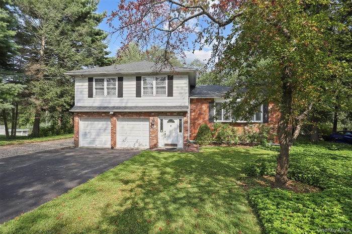 Split level home with brick siding, a garage, driveway, a front yard, and a shingled roof