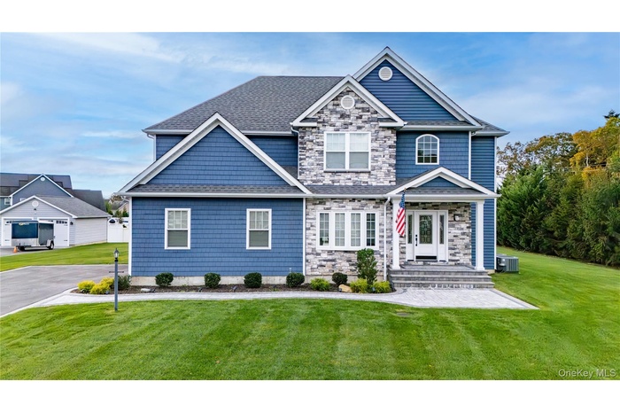 View of front of home featuring a front yard, a shingled roof, and stone siding
