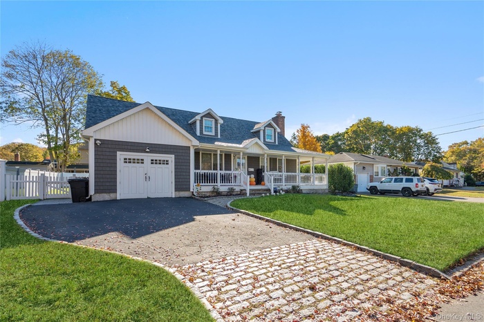 Cape cod home featuring covered porch, decorative driveway.