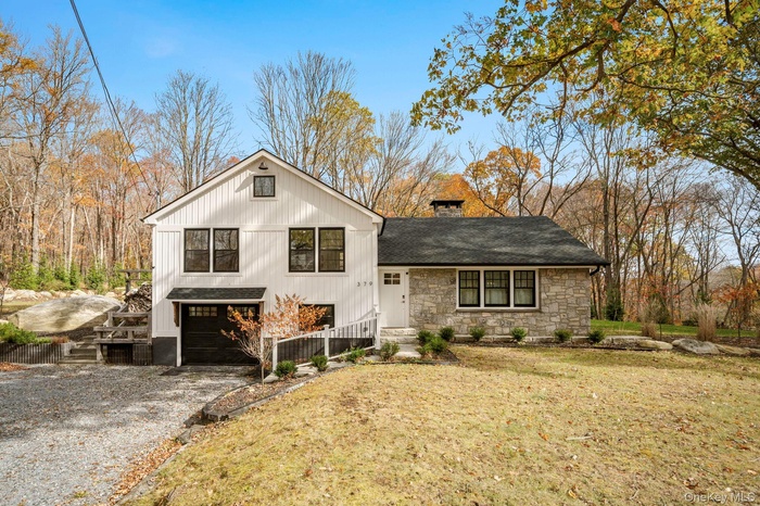 View of front of house with stone siding, a chimney, gravel driveway, a garage, and a front lawn