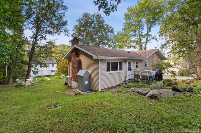 Back of property featuring a chimney, roof with shingles, and a yard