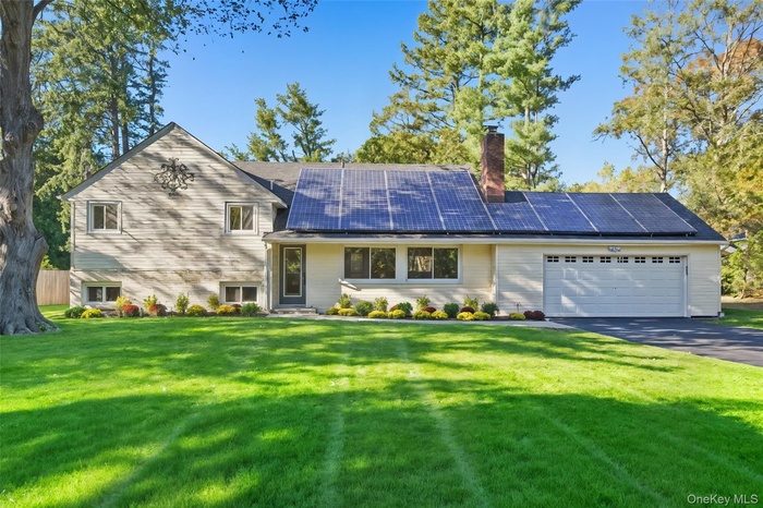 Tri-level home featuring solar panels, a chimney, a front lawn, driveway, and a garage