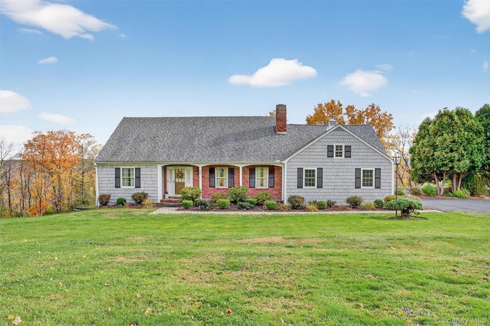 View of front facade featuring covered porch, a front lawn, a chimney, and roof with shingles