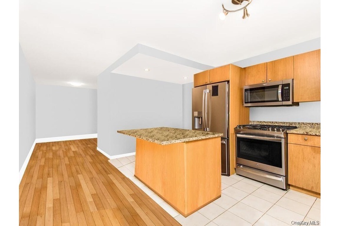 Kitchen featuring appliances with stainless steel finishes, light stone counters, a kitchen island, brown cabinetry, and light wood-type flooring