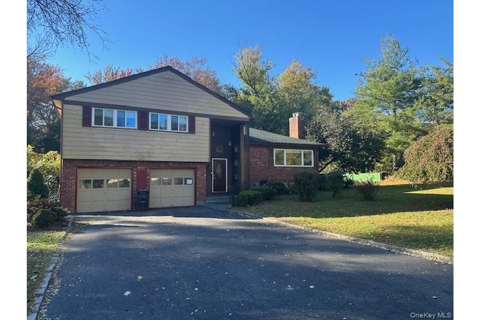 Tri-level home featuring brick siding, driveway, a chimney, an attached garage, and a front yard