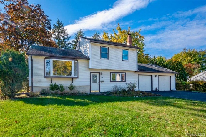 Tri-level home with a front yard, a chimney, an attached garage, and asphalt driveway