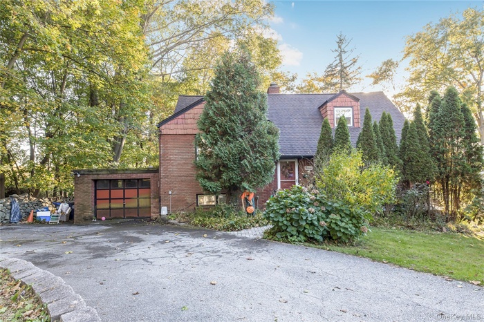 View of front facade with a chimney, a garage, asphalt driveway, brick siding, and roof with shingles