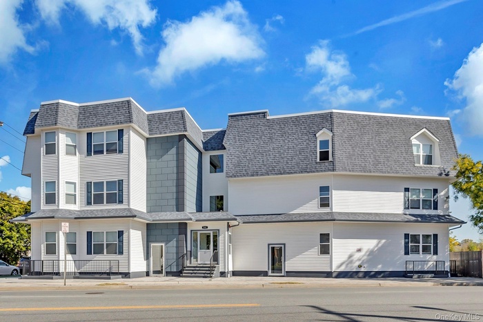 View of front facade featuring mansard roof and a shingled roof