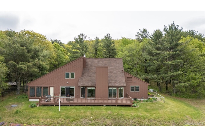 Back of house featuring a shingled roof, a wooded view, a yard, and a deck
