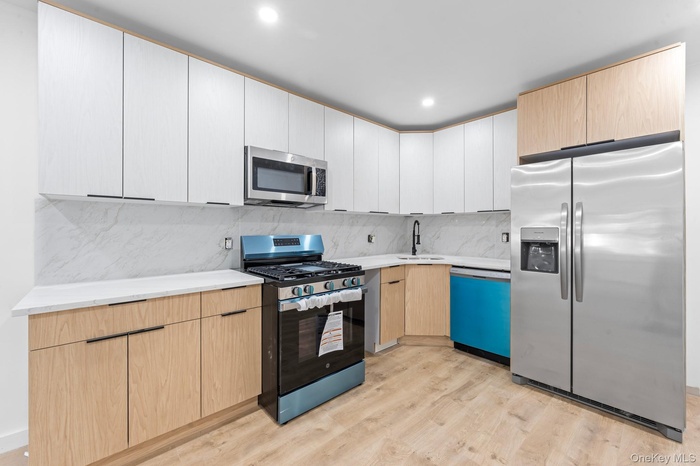 Kitchen with appliances with stainless steel finishes, light brown cabinetry, modern cabinets, light wood-type flooring, and decorative backsplash
