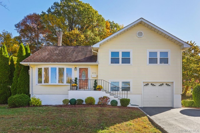 Split level home with a front lawn, an attached garage, driveway, and roof with shingles