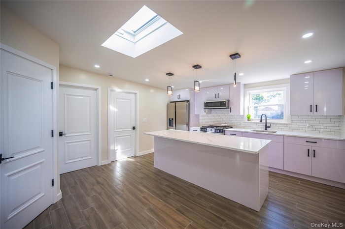 Kitchen featuring a kitchen island, stainless steel appliances, dark wood-style flooring, decorative light fixtures, and a skylight