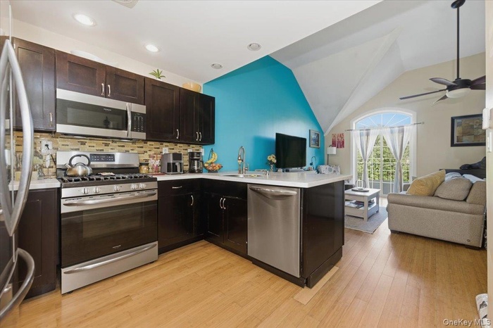 Kitchen with open floor plan, appliances with stainless steel finishes, decorative backsplash, a peninsula, and vaulted ceiling