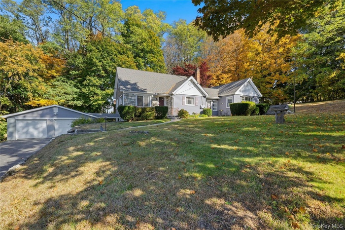 View of front of home featuring an outbuilding, a front yard, a chimney, and view of wooded area