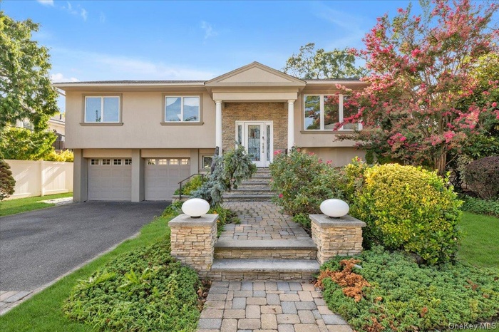 Split foyer home with an attached garage, asphalt driveway, stucco siding, and stone siding