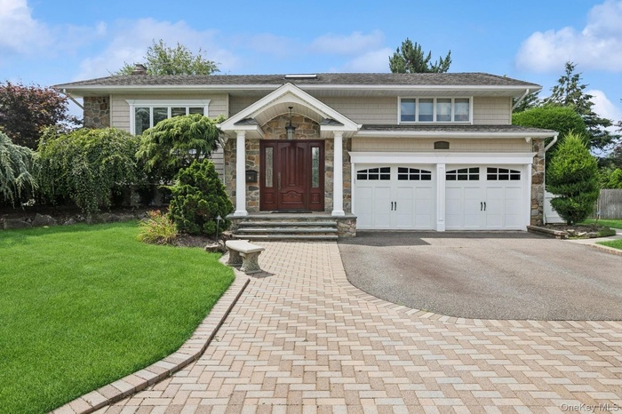 View of front of home featuring asphalt driveway, stone siding, a front yard, and a garage