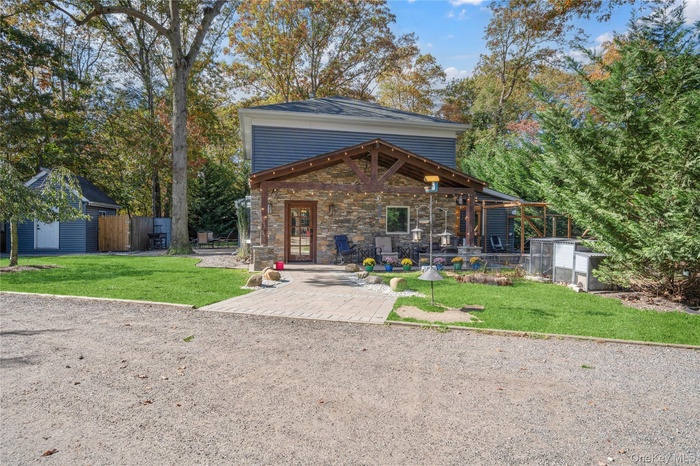 View of front of home with a patio area, stone siding, and view of scattered trees