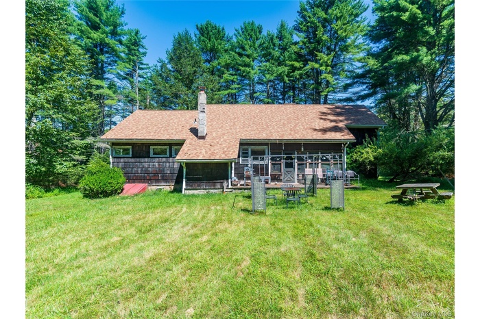 Rear view of property with a chimney, a lawn, a shingled roof, and view of scattered trees