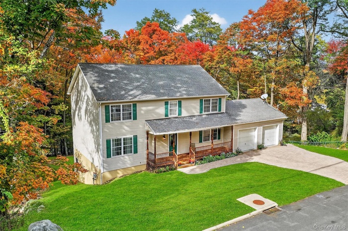 View of front of house with a front lawn, covered porch, driveway, an attached garage, and roof with shingles