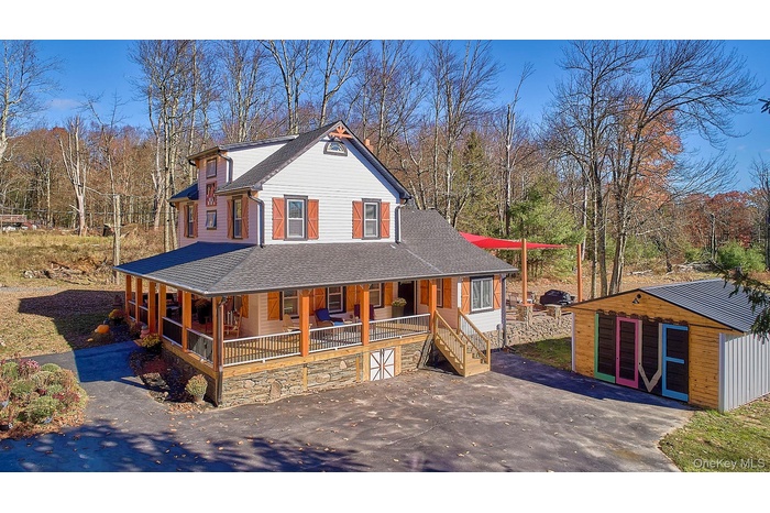 View of front facade with a large porch, an outbuilding, a shingled roof, and stairway