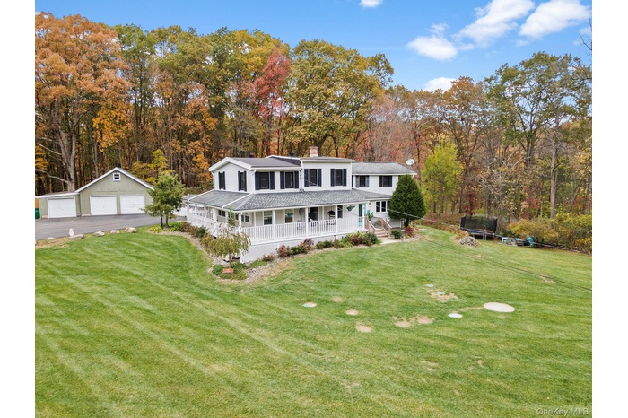 Rear view of house featuring a trampoline, a detached garage, a porch, an outdoor structure, and a chimney