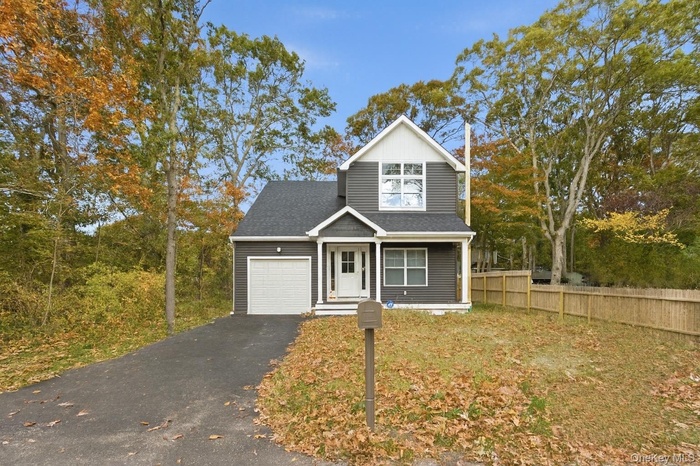 Traditional-style house featuring driveway, a shingled roof, covered porch, a garage, and view of wooded area
