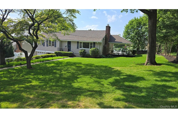 Ranch-style home featuring an attached garage, a chimney, and a front lawn