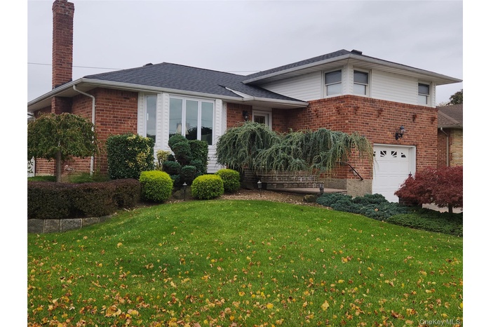 View of front of property with brick siding, a chimney, a front lawn, and a garage
