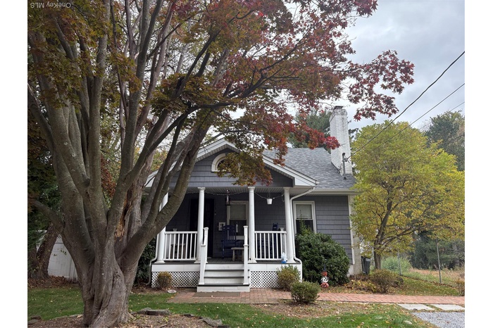 View of front of home featuring a porch, a chimney, and a shingled roof