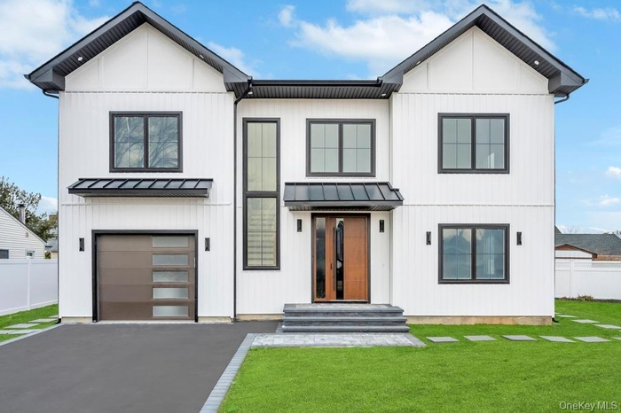 Modern farmhouse with a standing seam roof, an attached garage, driveway, and metal roof