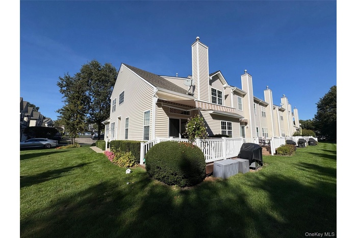 View of unit featuring a yard, a deck, a chimney, and roof with shingles