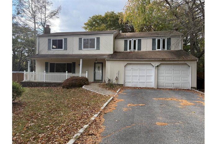 Traditional home featuring asphalt driveway, a chimney, covered porch, and a shingled roof