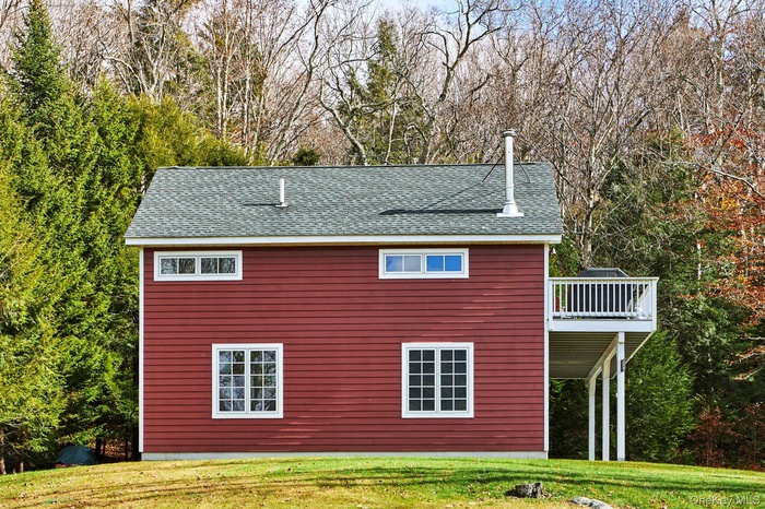 View of side of property featuring a yard, roof with shingles, and a deck