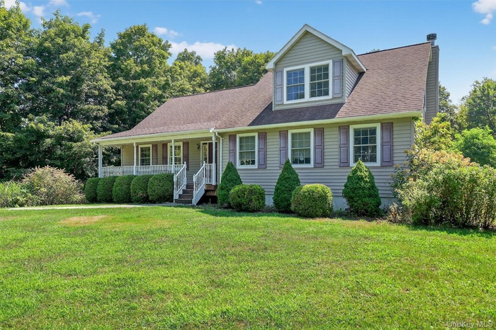 View of front of house featuring a porch, a front lawn, roof with shingles, and a chimney